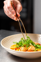 Chef plating pasta with herbs using precision tongs in a professional kitchen. Gourmet dish with...