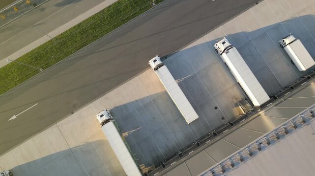 Aerial view of a logistics hub with four white trucks, ready for cargo distribution. The expansive warehouse features solar panels, emphasizing sustainable operations.