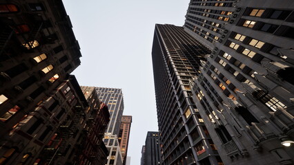 Obraz premium In a vibrant urban setting, towering skyscrapers loom overhead as the sun sets, casting a dramatic silhouette. The architecture showcases a blend of modern and classic designs, inviting exploration.