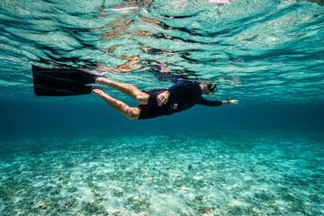 Caucasian Male snorkeler swimming in crystal turquoise waters with mask, snorkel, fins and black...