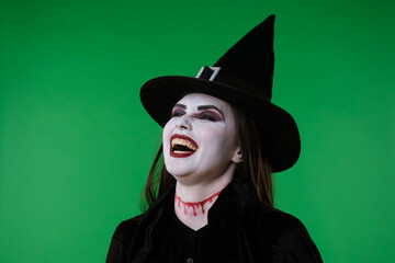 A witch with vampire makeup, in black cloak and hat, laughing eerily