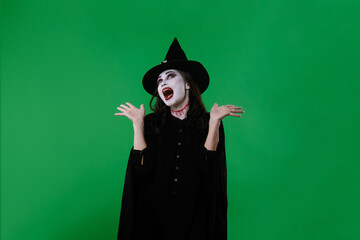 A witch with vampire makeup in a black cloak and hat, poses cheerfully
