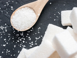 background of sugar cubes and sugar in spoon. White sugar on black background. Sugar cubes and granulated in wooden spoon