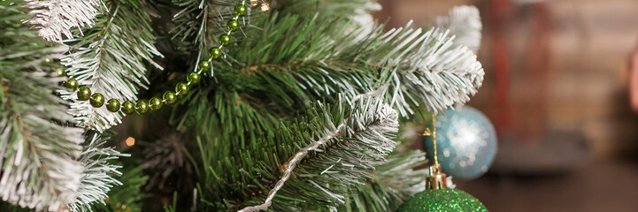 Close up of Christmas tree branches with festive ornaments, a green bead garland, and lights....
