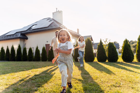 Happy children running in the garden of a sustainable house with solar panels