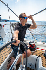 Man at the helm of a sailing yacht near Croatia, steering the boat through open water. Leadership,...