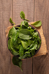 Green baby spinach leaves in wooden bowl on wooden background. Organic food concept. 