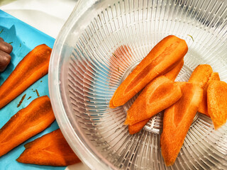 Chopped orange carrots placed in a colander after slicing on a blue cutting board in a bright...