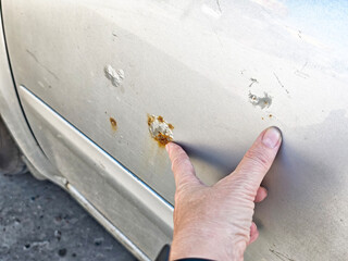 Car door damaged by rust spots in an urban area during daylight hours