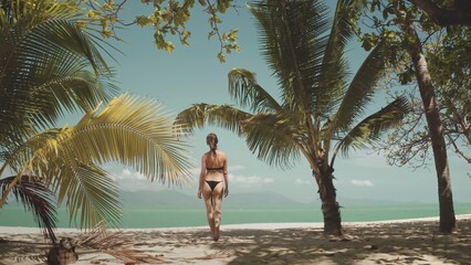 Young woman is enjoying her vacation walking on a white sand beach surrounded by palm trees with turquoise water in the background