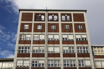 Facade of an urban building with red brick elements, rectangular windows, and arched openings on the top floor under a partly cloudy sky.