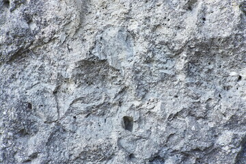 Close-up of rough stone wall texture with natural holes and cracks. Abstract rocky surface background with detailed structure.