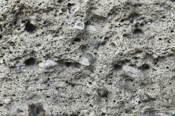 Close-up of rough stone wall texture with natural holes and cracks. Abstract rocky surface background with detailed structure.