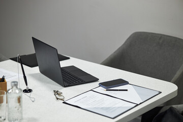 Modern office workspace featuring open laptop, smartphone, documents, pen, eyeglasses and water bottle on desk, suggesting professional business environment without employees present