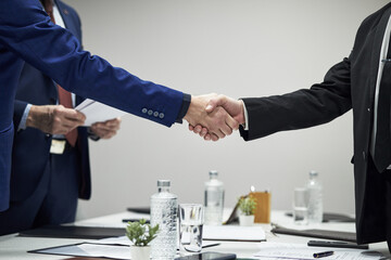 Unrecognizable male business partners shaking hands in office setting, corporate professionals...