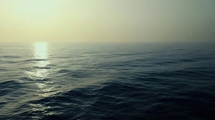 Obraz premium Serene expanse of the ocean under a hazy sky with sunlight reflections dancing on surface