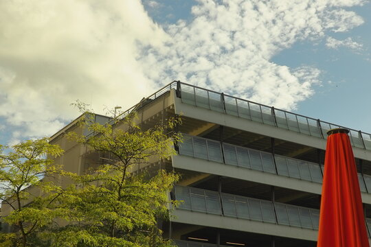 Modern building with glass facade and green trees in front, church tower with clock in the background under blue sky with clouds.