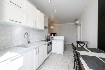 bright kitchen features white cabinets, subway tile backsplash, and marble-patterned floors. A...
