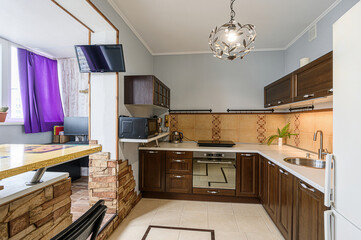 cozy kitchen with dark wood cabinets, light countertops, and tan tile backsplash. A unique light fixture hangs overhead