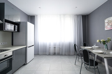 modern, gray-toned kitchen with a dining area featuring a table set for four. A large window with...
