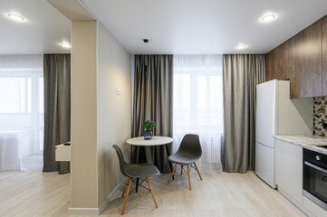 Fototapeta premium cozy interior featuring a dining set by the window, with modern design chairs, a round table with a vase, and a well-lit kitchen area