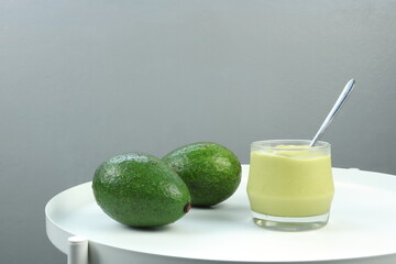 a glass of cool fresh avocado smoothie juice is on white table with organic avocados displayed in...
