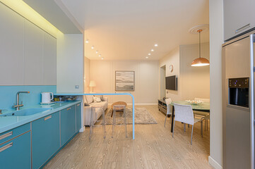 modern apartment interior with a turquoise kitchen, open to a living area with wood floors and warm...