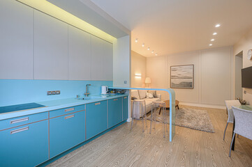 modern apartment with a turquoise kitchen merging into a living area. Light walls and wood floors enhance the open space