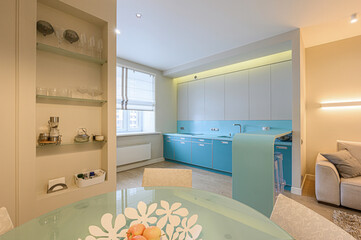 Modern kitchen with turquoise cabinets and a glass table. Display shelves feature glassware