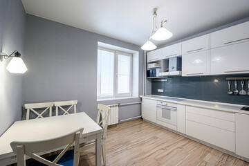 well-lit, modern kitchen with white cabinets, a gray wall, and a light wood floor. A white table...