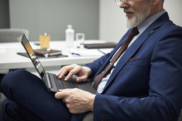 Middle aged Caucasian man sitting at desk using laptop computer in office setting, wearing suit and...