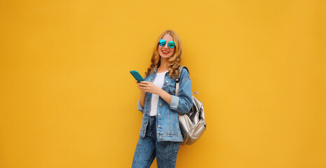 Happy young woman student with phone, modern smiling girl holding smartphone on yellow background