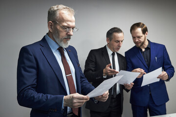 Three middle aged Caucasian men standing together reviewing documents, two colleagues discussing...