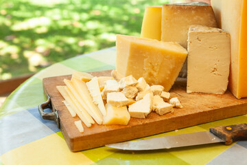 Assortment of sliced and chunked cheeses with knife on wooden cutting board