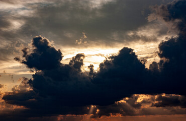 Sunset in a dramatic sky with the rays of a dream piercing through the dark clouds against the background of the city. Bright epic sky. Dramatic evening light and fiery orange sunset