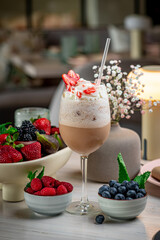 Berry milkshake delight. A tasty milkshake with strawberries sits beside fresh berries and a vase, creating a cozy dining vibe.