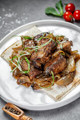 Savory grilled meat served with onions. Grilled meat pieces served on a plate with onions and garnished with green herbs, accompanied by cherry tomatoes.