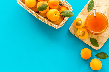 Summer preserves. Apricot jam in jar near fresh fruits on blue background top view frame space for text