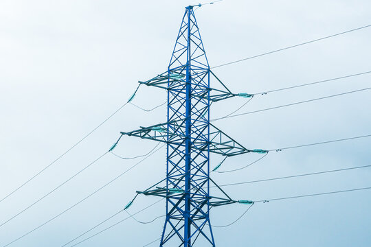 High voltage electrical power line tower structure against a clear sky. Blue lattice utility pole distributing electricity. Energy grid transmission for modern infrastructure. - Powered by Adobe