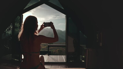 Capturing the sunset view of a mountain range from a bungalow in thailand, a woman enjoys her vacation, sharing moments of happiness and inspiration on social media