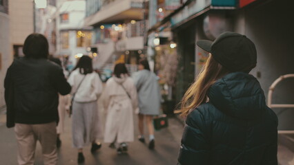 Stylish blonde woman leads her friends through tokyo's bustling streets, exuding a modern vibe in a black cap and jacket