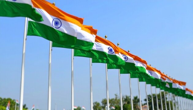 Row of Indian flags fluttering on tall flagpoles against clear sky, with wind turbines in background