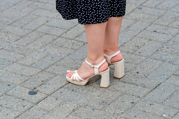 Woman legs wearing beige block heel sandals with ankle strap standing on urban brick pavement in...
