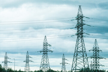 Row of tall electricity pylons and power lines against a cloudy sky. Electrical energy supply and...