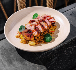 Delicious grilled duck pieces served on a plate with flavorful rice on a table