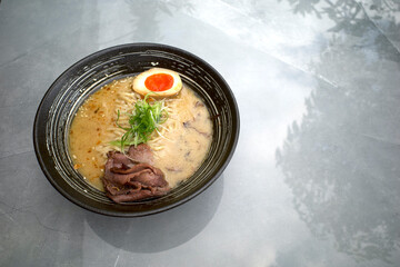 Japanese ramen soup with vegetables, chicken egg, noodles, broth in a bowl on a grey table