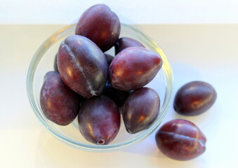 Ripe purple plums of the Ugorka variety in a transparent glass plate on a white background. top view