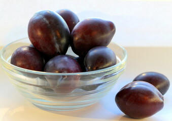Ripe purple plums of the Ugorka variety in a transparent glass plate on a white background