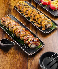 Sushi rolls on black plates with sauce on a wooden table
