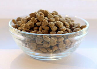 Dry balanced food for cats or dogs in a glass transparent bowl on a white background.